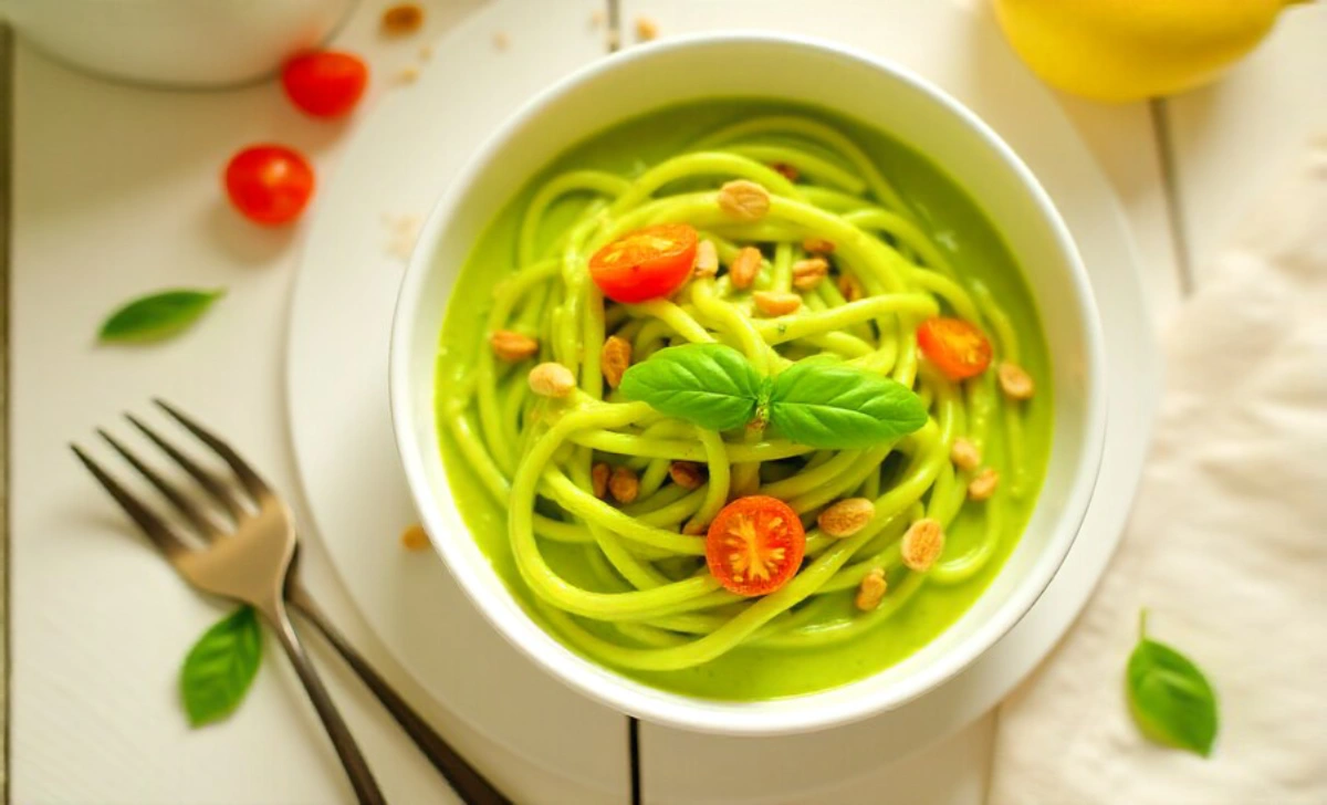 Creamy avocado pasta recipe with cherry tomatoes and pine nuts in white bowl on wooden table