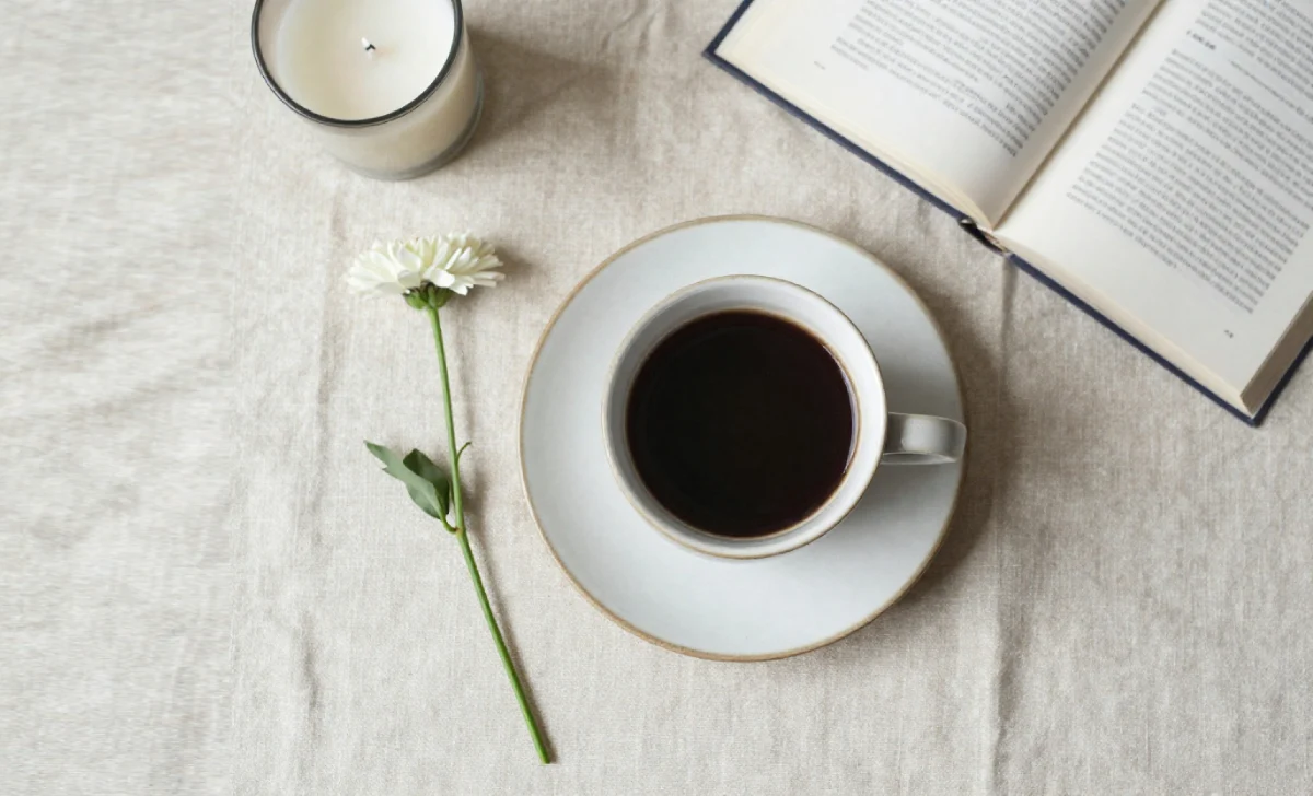 Ceramic coffee cup on a linen cloth with a candle and fresh flower representing the bougiebunna morning ritual